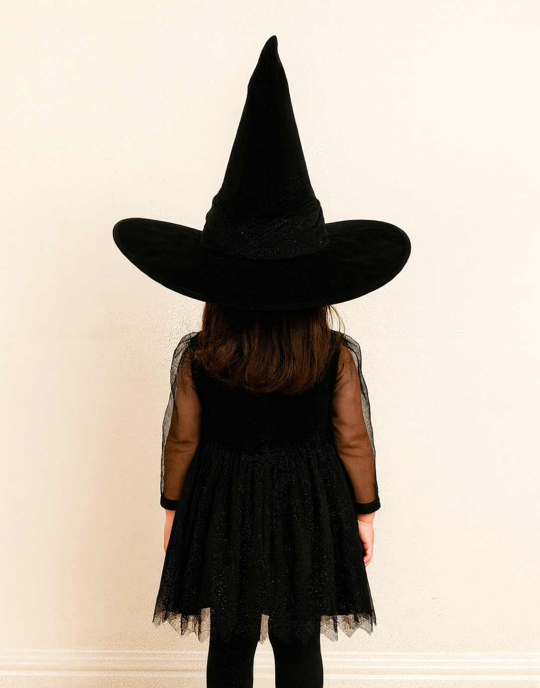 Back view of person wearing a black witch costume with a pointed Witch Hat on a plain background.