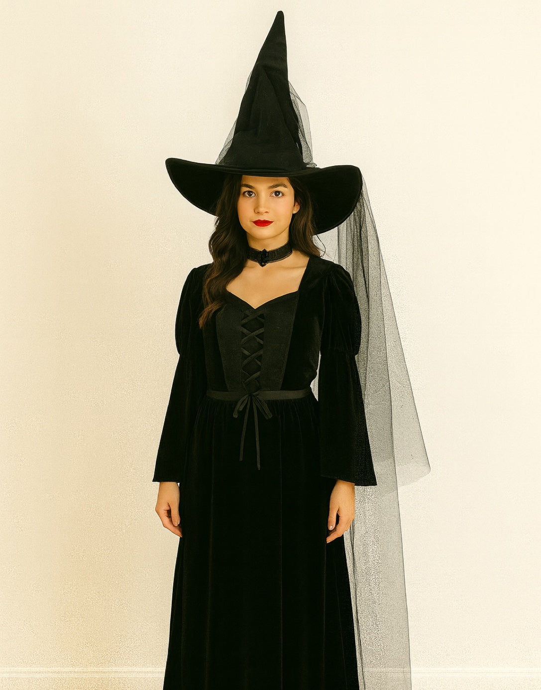 Person wearing a black witch costume with a pointed Witch Hat and long dress on a beige background.