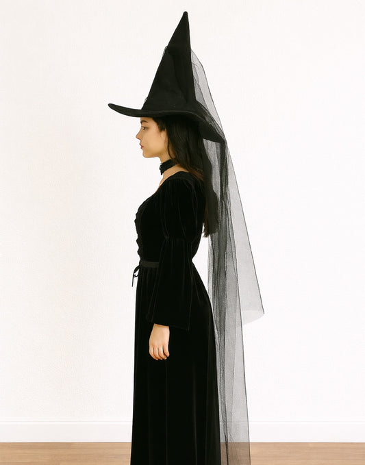 Side view of woman wearing a black witch costume with a pointed Witch Hat and long dress on a white background
