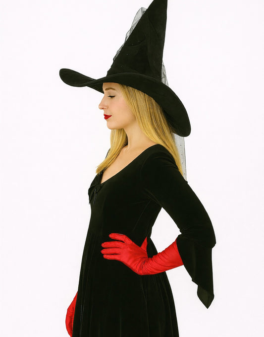 Side view of woman wearing a black witch costume with a hat, dress, and red Witch Long Gloves on a plain background