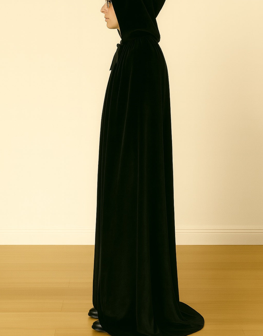 Side view of person wearing a black Wizard Robe standing against a beige wall.