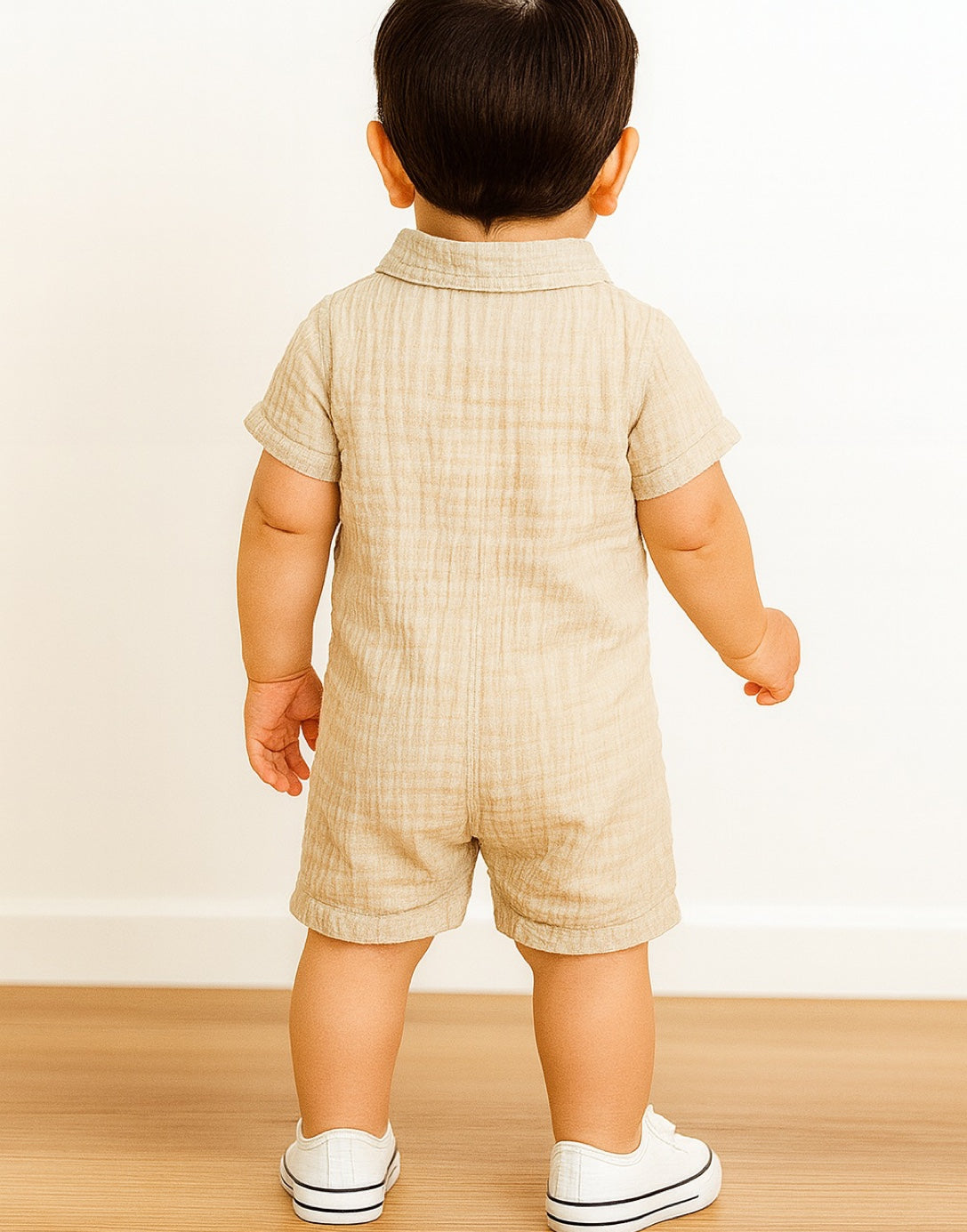 Back view of baby boy wearing a beige flap pocket shirt romper with a collar and short sleeves.