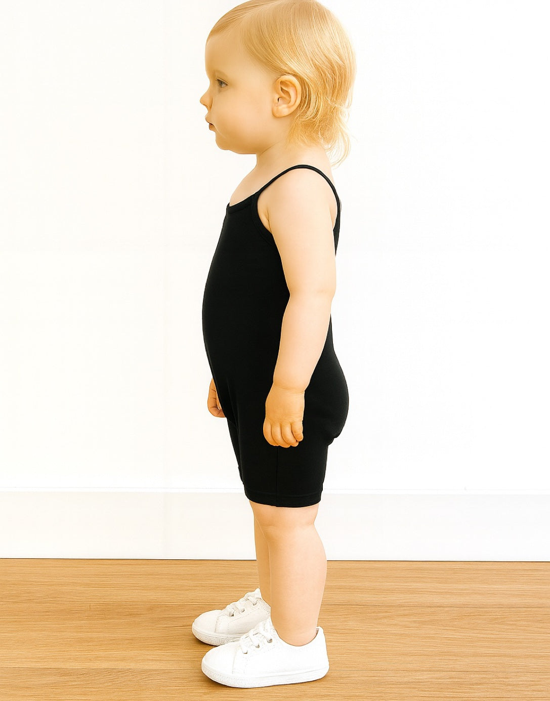 Side view of child wearing a black Cami Unitard Romper on a white background.