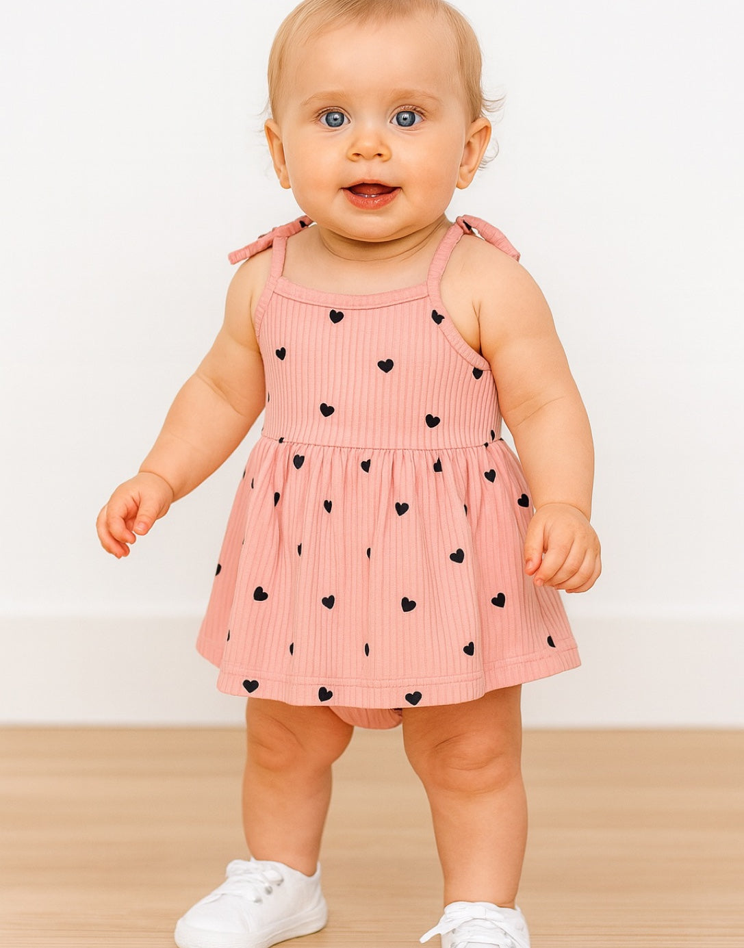 Baby wearing a pink Baby Girl Cami Bodysuit Dress with black heart patterns on a white background.