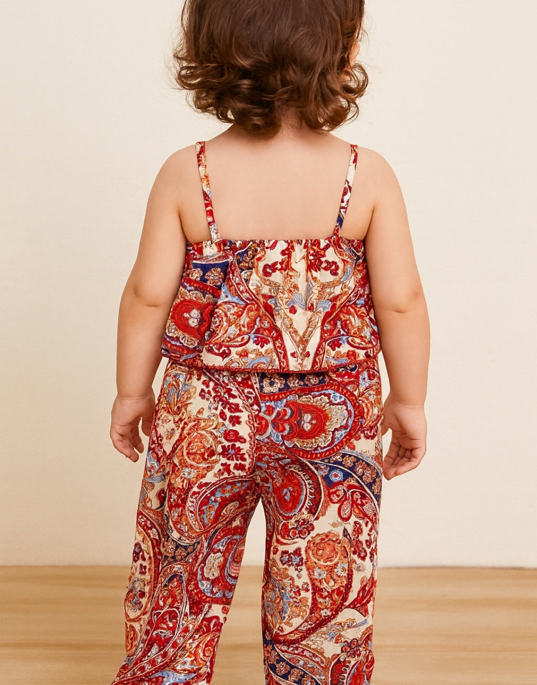 Back view of child wearing a colorful paisley Baby Girl Ruffle Hem Cami Top and Wide Leg Pants Set on a beige background