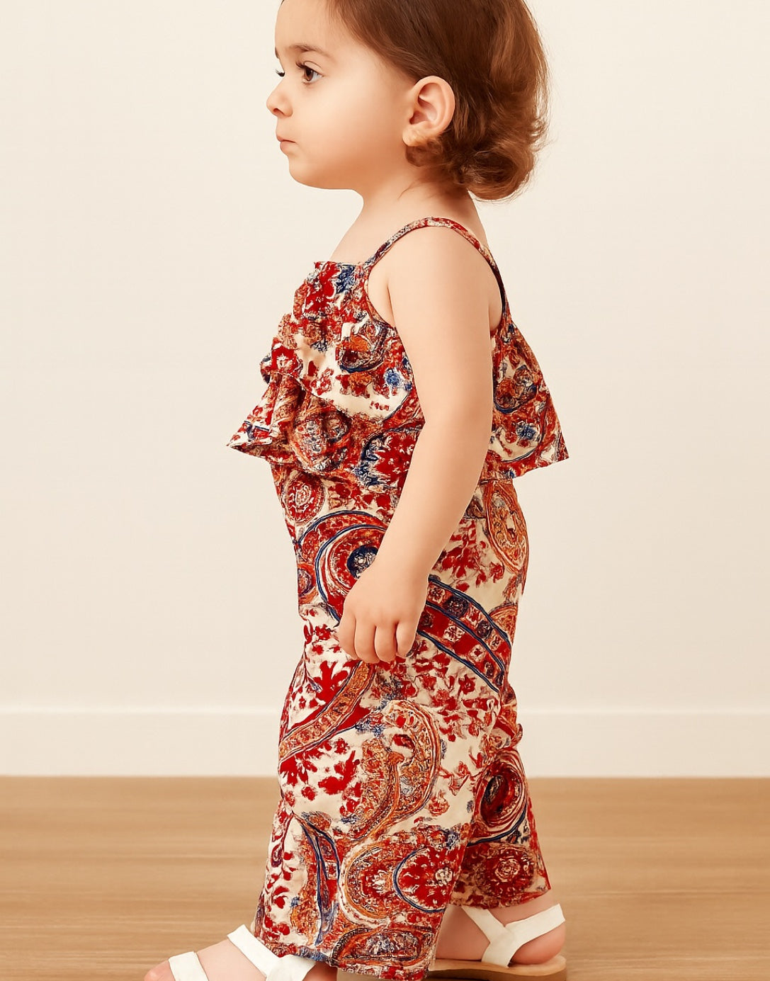 Side view of child wearing a red and beige patterned Ruffle Hem Cami Top and Wide Leg Pants Set on a wooden floor with a beige wall background