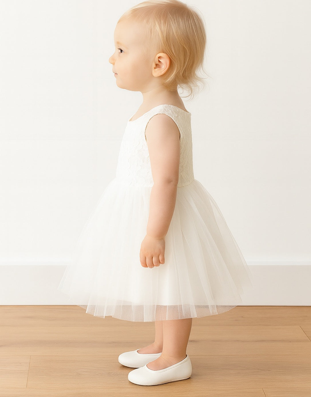 Side view of a baby wearing a white Sleeveless Party Dress with floral details on a plain background