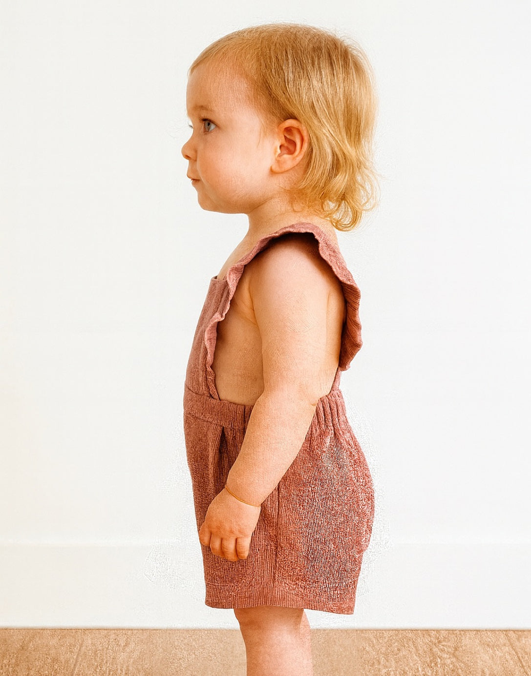 Side view of child wearing a pink romper with ruffled sleeves on a white background