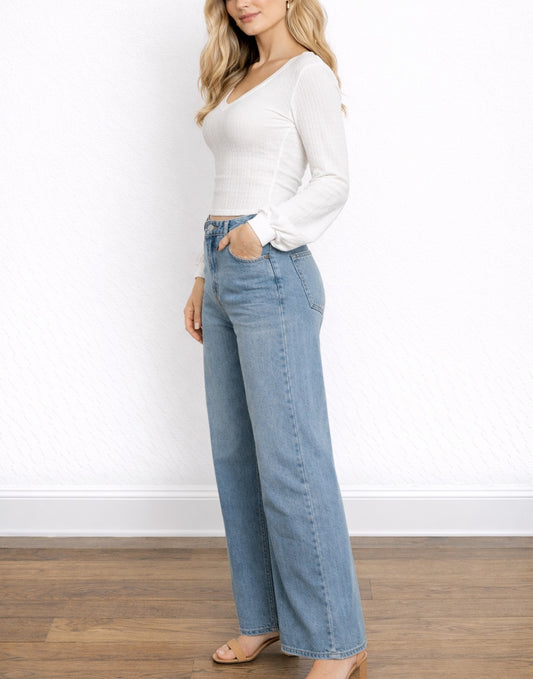Side view of woman wearing a white Bishop Sleeve Top and blue jeans against a white wall.