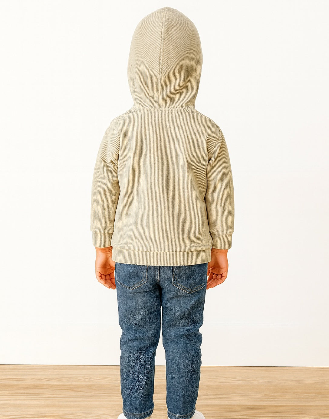 Back view of child wearing a beige hooded jacket and blue jeans on a white background