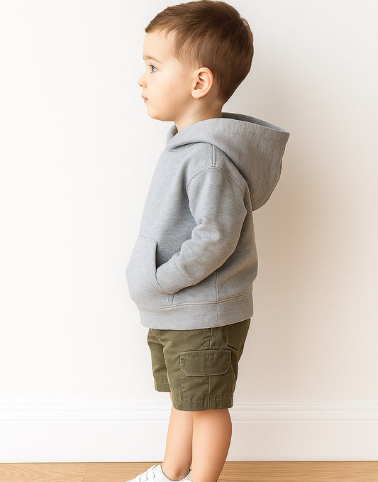 Side view of young boy wearing a gray hoodie and green shorts against a white wall.