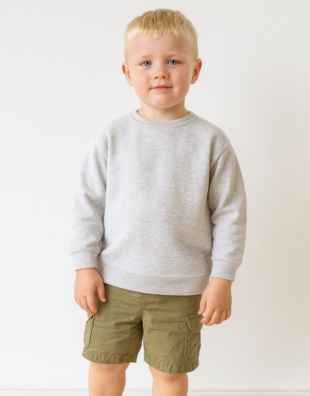 Young boy wearing a gray sweatshirt and green shorts on a white background