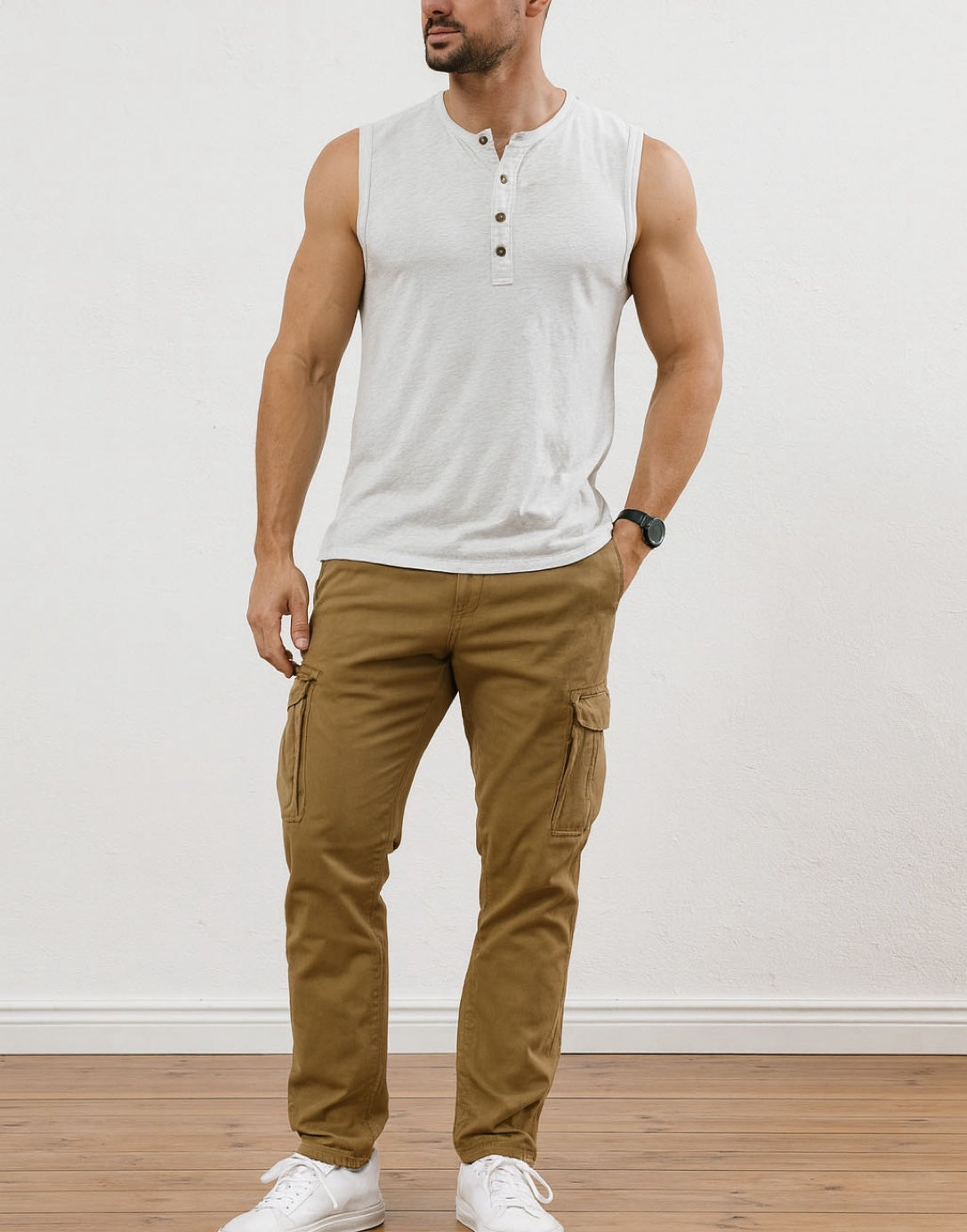 Man wearing a white Button Front Round Neck Tank Top and brown pants standing against a plain white wall.