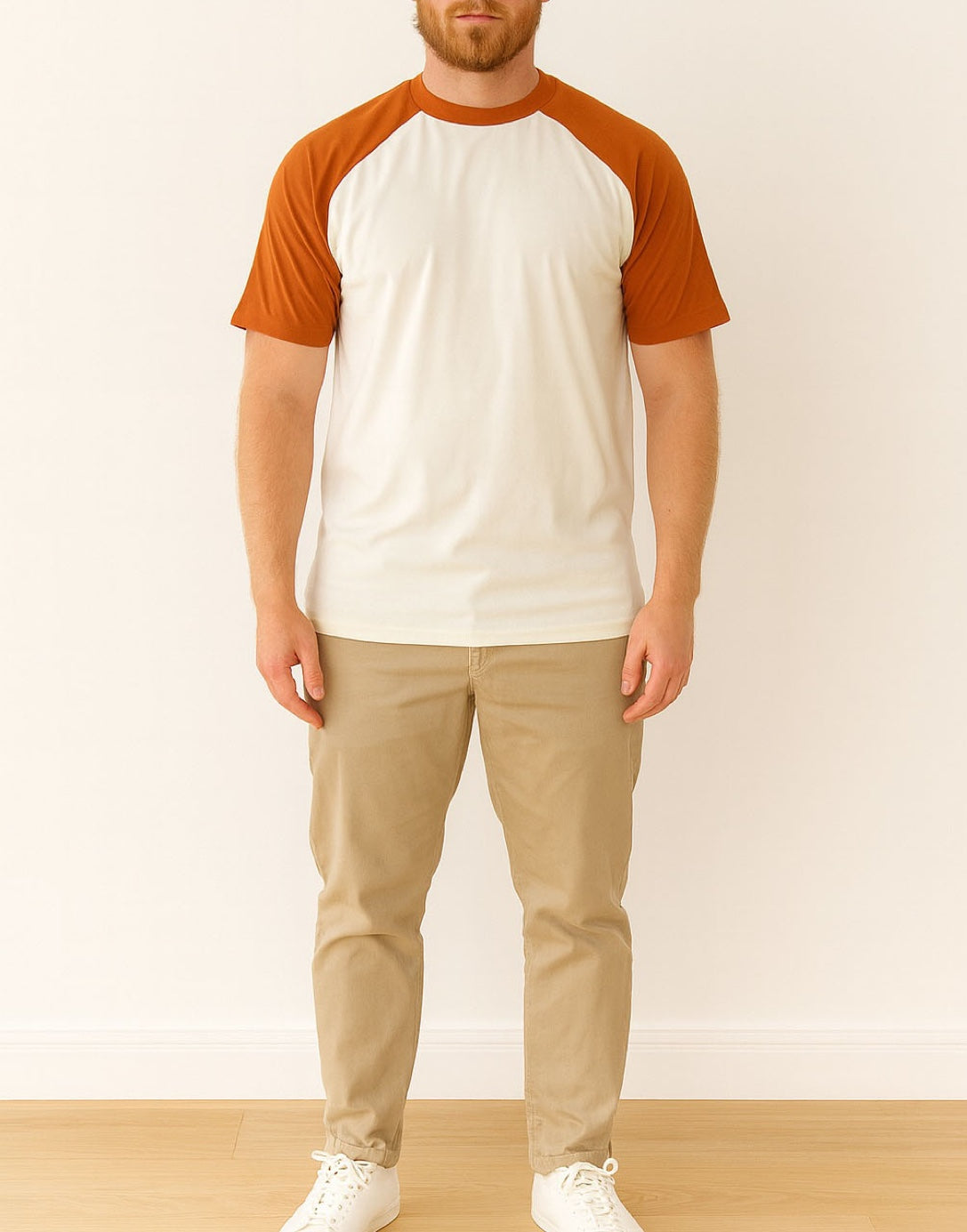 Person wearing a white and orange Crew Neck Raglan Short Sleeve T-Shirt with beige pants on a plain background