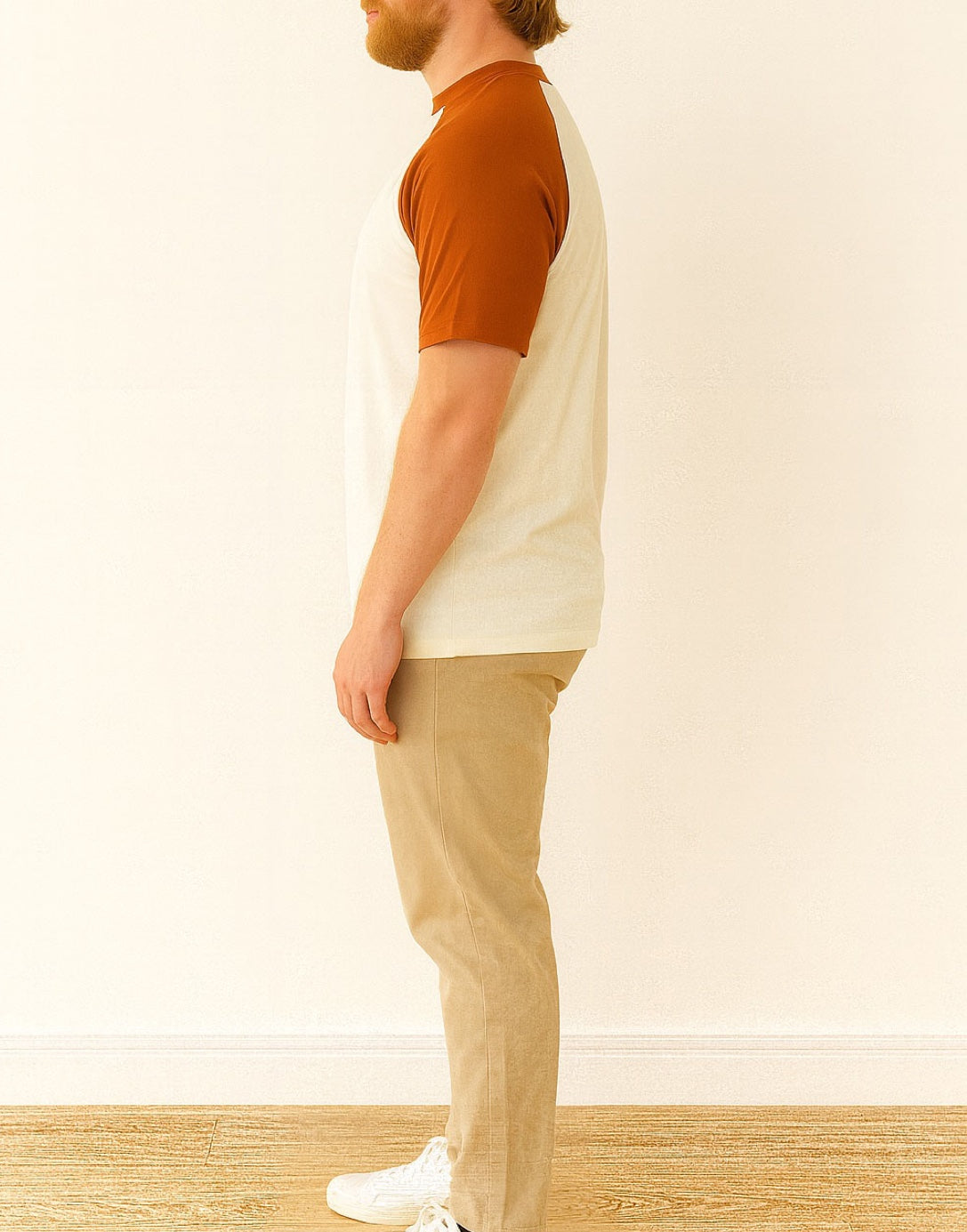Side view of person wearing a brown and beige Crew Neck Raglan Short Sleeve T-Shirt with beige pants standing against a white wall.