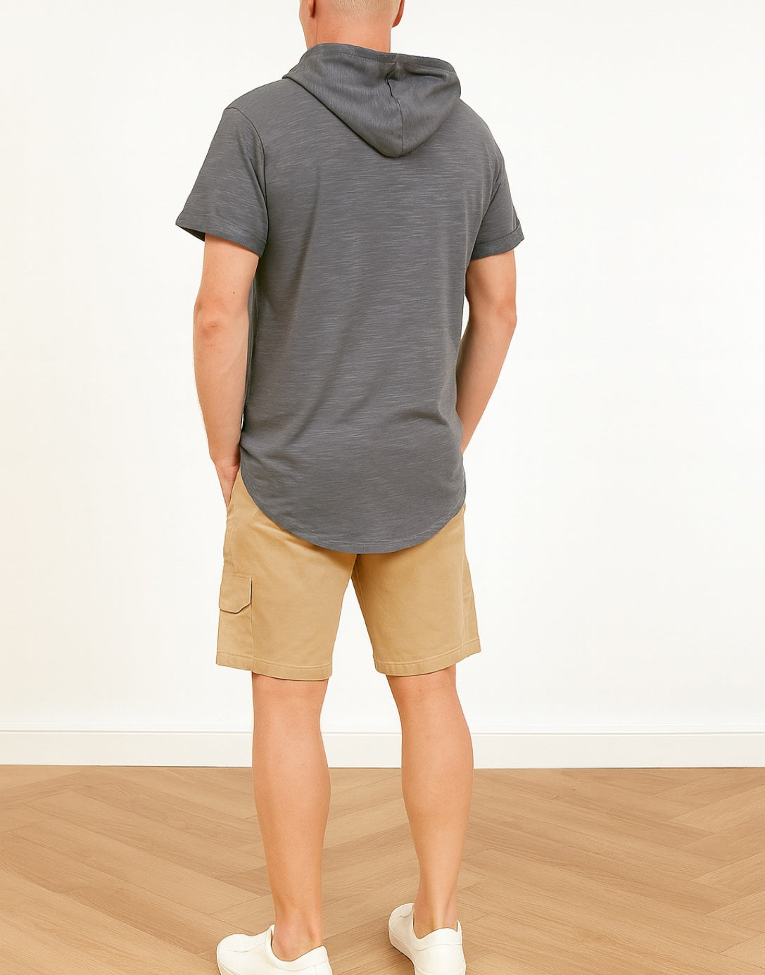 Back view of person wearing a gray hooded tee shirt and beige shorts on a white background.