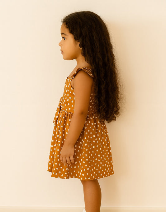 Side view of young girl wearing a polka dot Bow Front Cami Dress against a plain background.