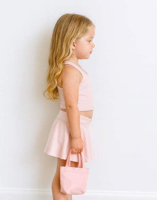 Side view of young girl in a pink Crop Top and Skort Set holding a matching bag against a white background.