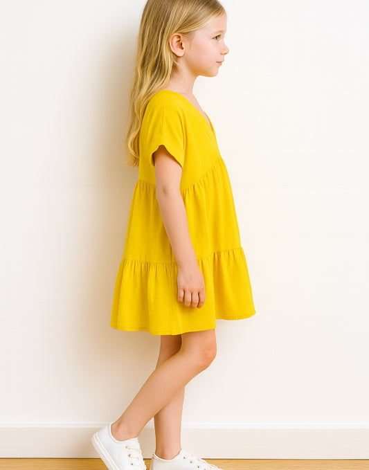 Side view of young girl wearing a yellow Gathered Smock Dress against a white background.