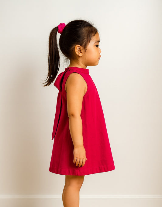 Side view of young girl wearing a pink Halter Tie Back Mini Dress.