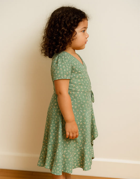 Side view of young girl wearing a green floral Maxi Wrap Dress on a plain background.