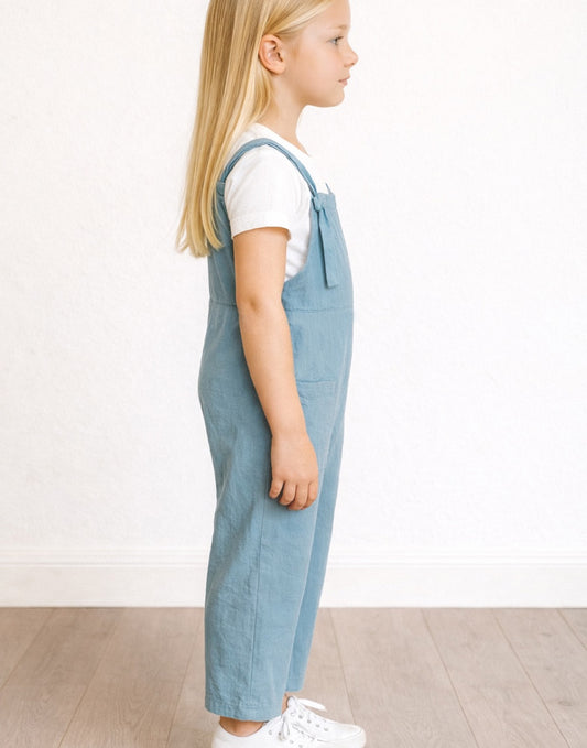 Side view of young girl wearing blue overalls and a white shirt on a plain background.