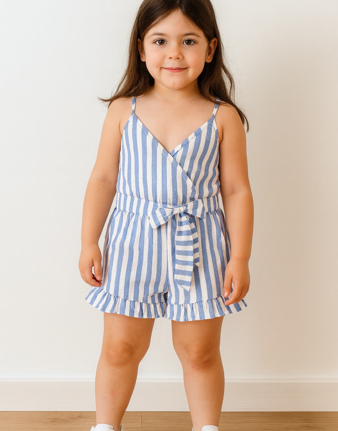 Young girl wearing a blue and white striped Ruffle Hem Belted Cami Romper against a plain background