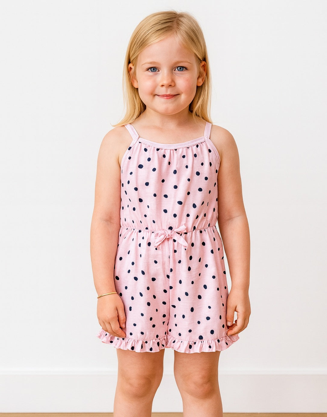 Young girl wearing a pink Ruffle Hem Cami Romper with black polka dots on a white background