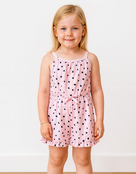 Young girl wearing a pink Ruffle Hem Cami Romper with black polka dots on a white background