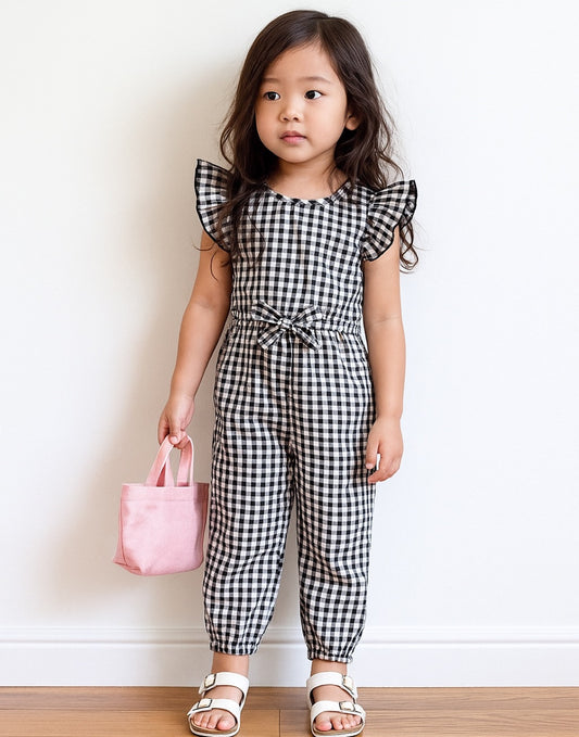 Young girl wearing a black and white checkered Ruffle Sleeve Jumpsuit holding a pink bag against a plain background