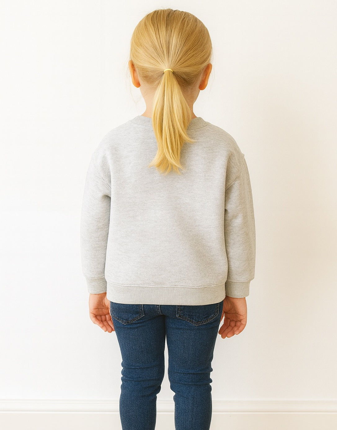 Back view of person wearing a gray sweatshirt and blue jeans with blonde hair in a ponytail on a white background