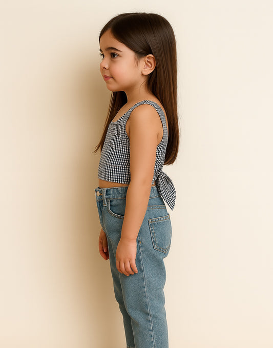 Side view of young girl wearing a checkered Tie Back Crop Top and jeans against a beige background