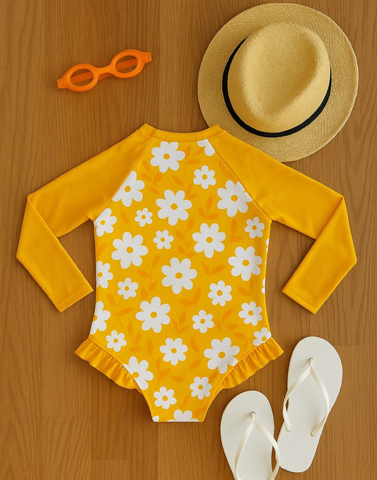 Back view of yellow swimsuit with white floral pattern, straw hat, orange sunglasses, and white sandals on a wooden surface.