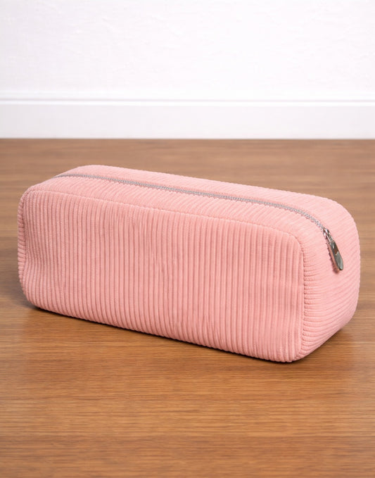 Side view of pink corduroy Makeup Bag on a wooden surface with a white background.