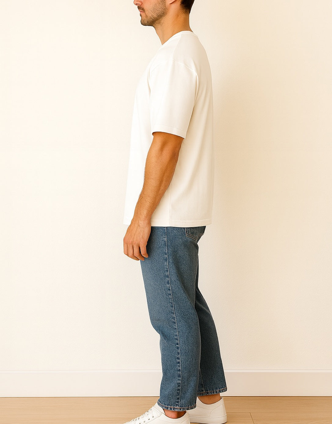 Side view of person wearing a white Oversized Longline Tee Shirt and blue jeans standing against a plain background