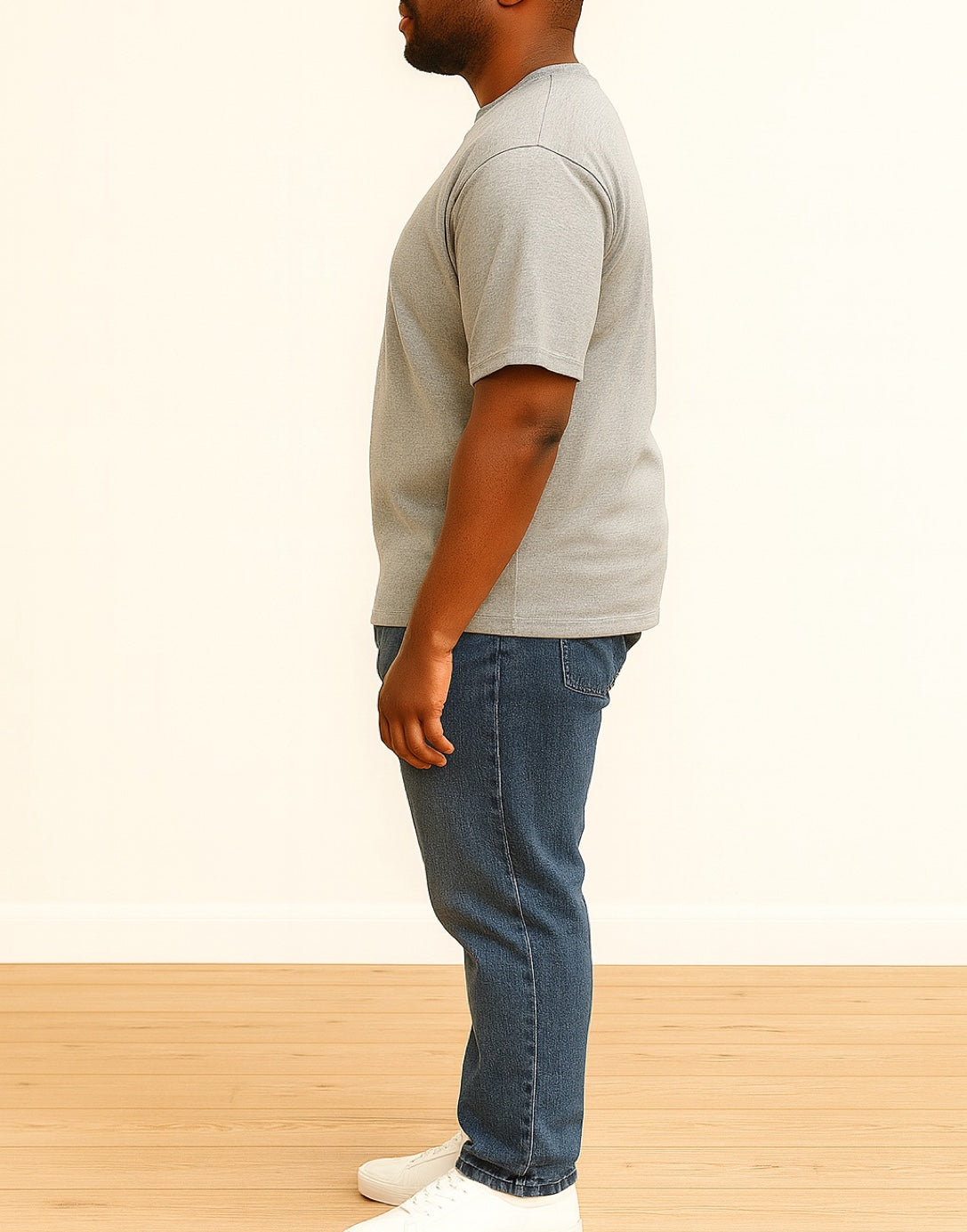 Side view of man wearing a gray Oversized Tee Shirt and blue jeans standing on a wooden floor with a white background