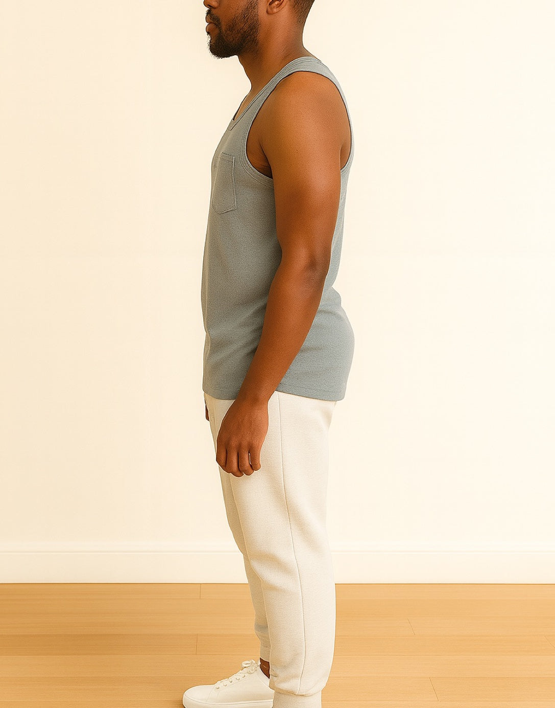 Side view of man wearing a gray Round Neck Pocket Tank Top and white pants standing against a plain background