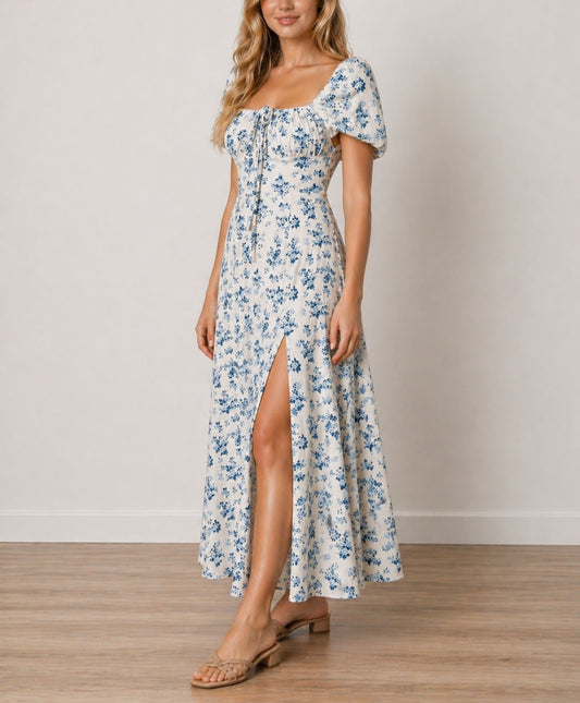 Side view of woman wearing a floral Milkmaid Front Tie Maxi Dress with a slit on a plain background