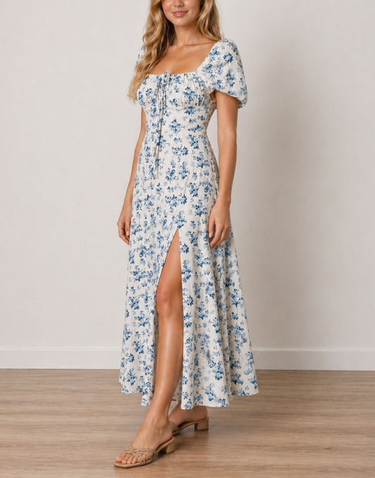 Side view of woman wearing a floral Milkmaid Front Tie Maxi Dress with a slit on a plain background