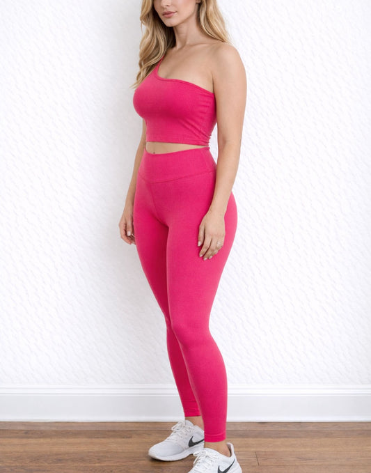 Side view of woman wearing a pink strapless One Shoulder Crop Top and leggings with white sneakers against a white wall.