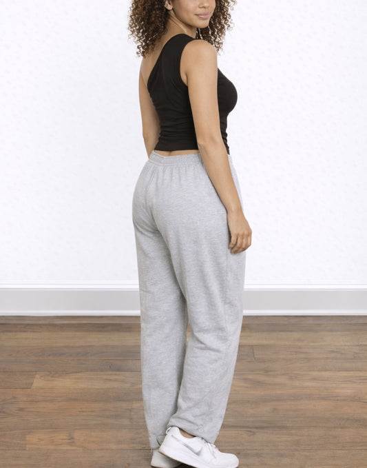 Side view of woman wearing a black One Shoulder Ruched Crop Tank Top and gray sweatpants on a white background.