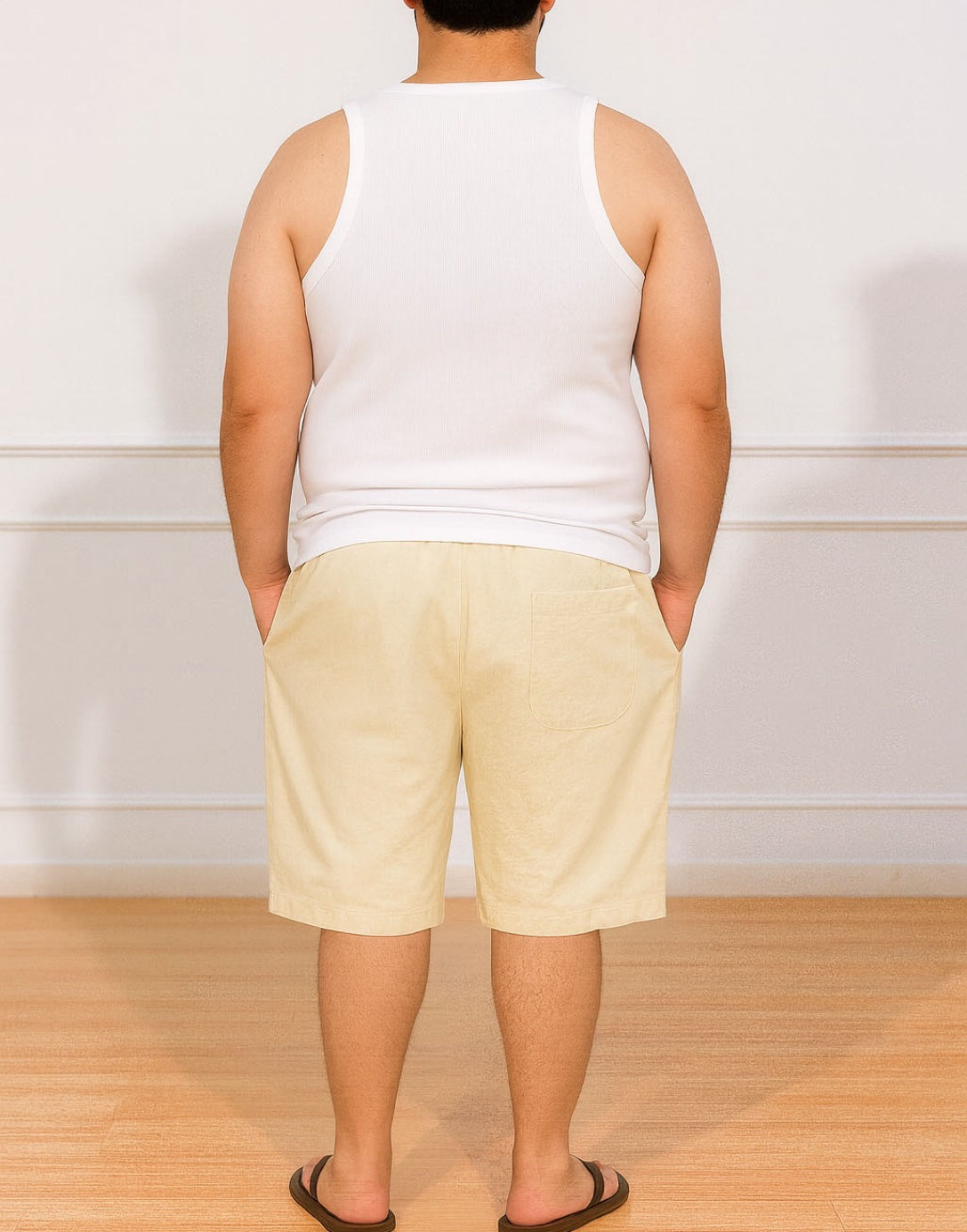 Back view of person wearing a white tank top and beige Plus Size Drawstring Knee Length Shorts standing against a plain white wall.
