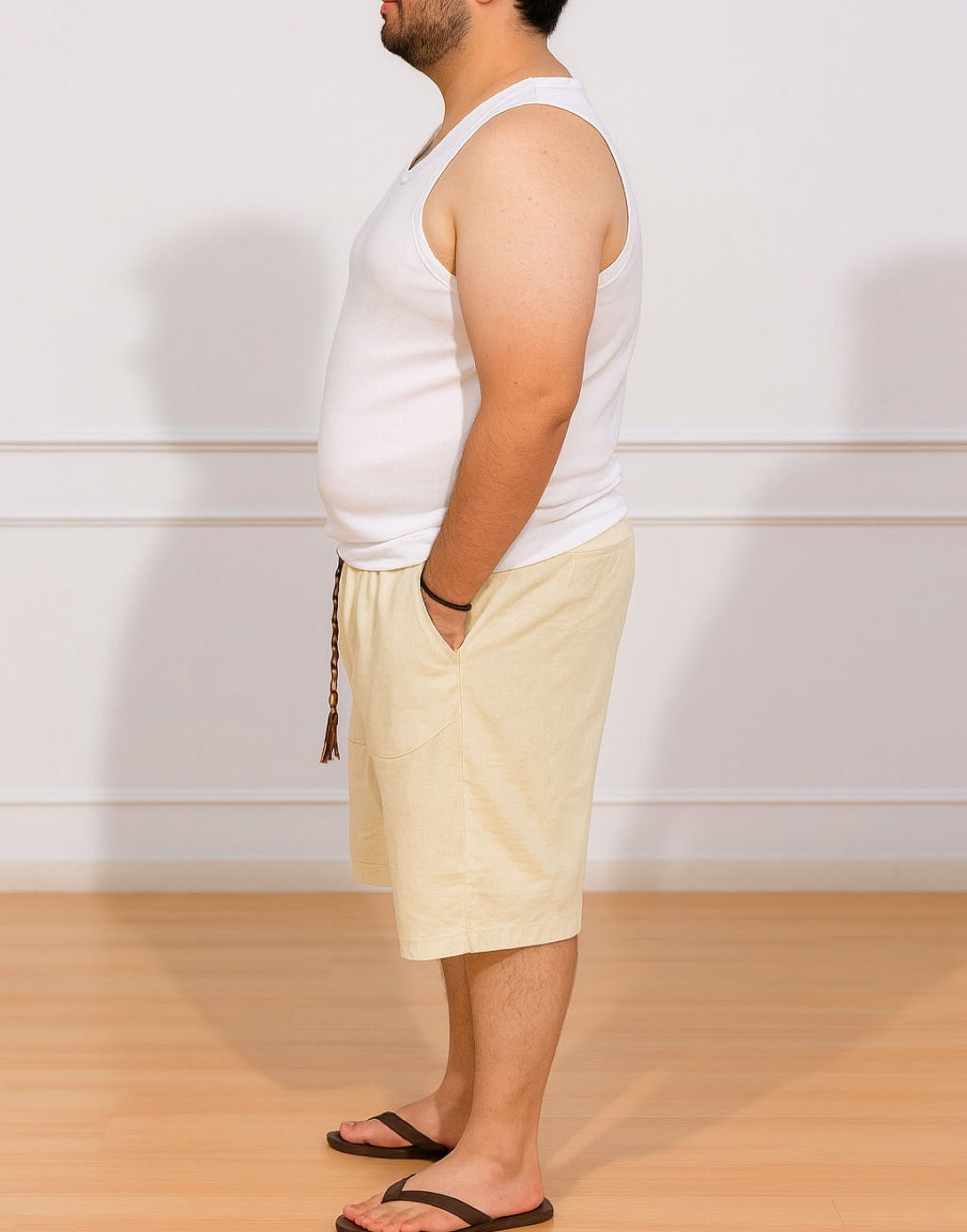 Side view of person wearing a white tank top and beige Plus Size Drawstring Knee Length Shorts standing against a plain white wall.