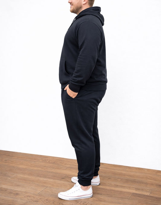 Side view of person wearing a black Plus Size Mens Classic Hoodie and pants with white sneakers on a wooden floor.
