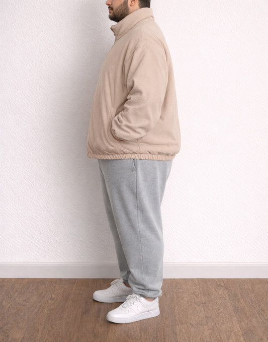 Side view of person wearing a beige Plus Size Mens Puffer Jacket and gray pants standing against a white wall..