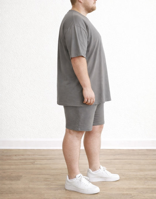 Side view of person wearing a gray T-Shirt and Biker Shorts Set with white sneakers on a plain background
