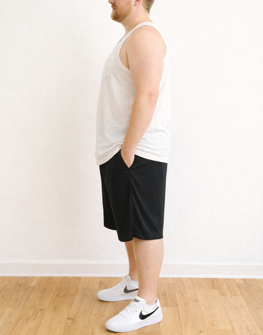 Side view of person wearing a white Plus Size Round Neck Pocket Tank Top and black shorts standing against a plain wall.