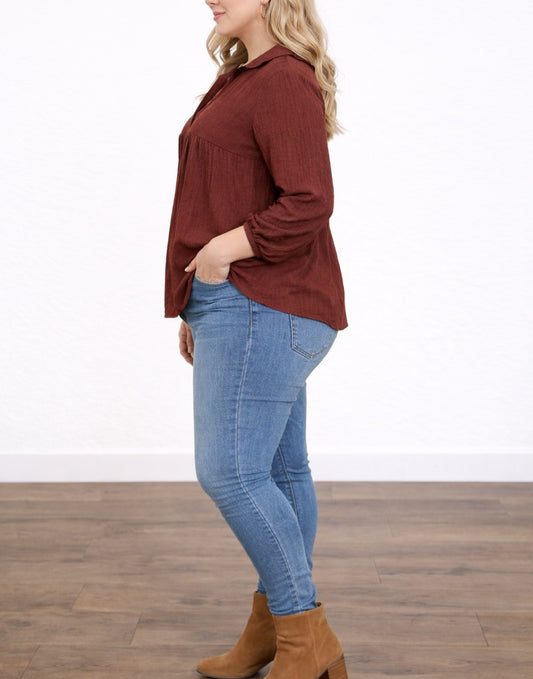 Side view of woman wearing a rust-colored Plus Size Long-Sleeve Top and blue jeans on a wooden floor.