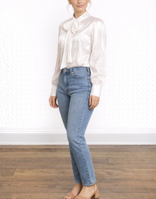 Side view of woman wearing a white Tie Neck Puff Long Sleeve Blouse with a bow and blue jeans on a plain background.