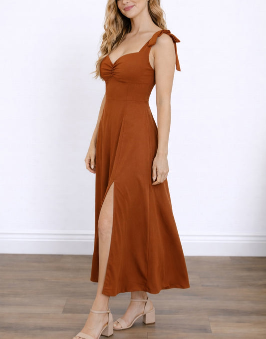 Side view of woman wearing a rust-colored Tie Shoulder Cami Corset Midi Dress with a slit on a white background.